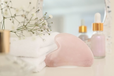 Photo of Rose quartz gua sha tool, skin care product and flowers on white table