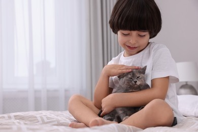 Cute little boy with kitten on bed at home. Childhood pet