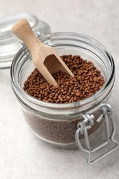 Photo of Glass jar with wooden scoop and buckwheat tea granules on light grey table, closeup