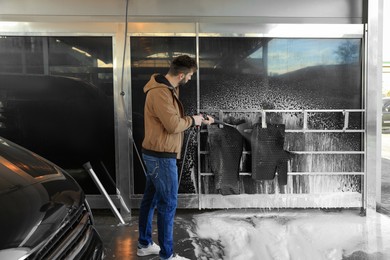 Man cleaning auto mats with high pressure water jet at self-service car wash