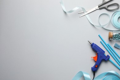 Photo of Hot glue gun and handicraft materials on grey background, flat lay. Space for text