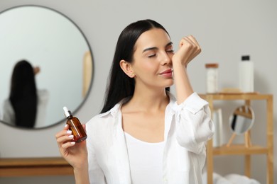 Photo of Young woman smelling essential oil on wrist indoors