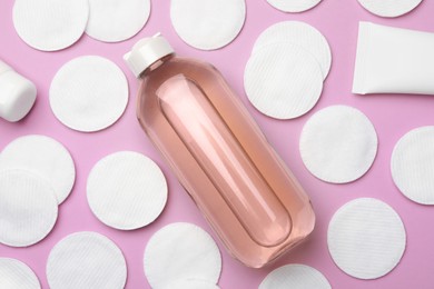 Bottle of micellar water and cotton pads on pink background, flat lay