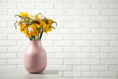 Beautiful blooming freesias in pink vase on table against white brick wall. Space for text