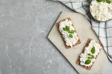 Photo of Crispy crackers with cottage cheese and basil on light grey marble table, flat lay. Space for text