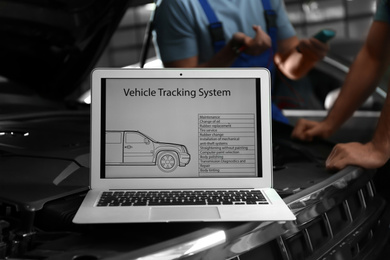 Laptop with vehicle tracking system and blurred mechanics on background. Auto diagnostic
