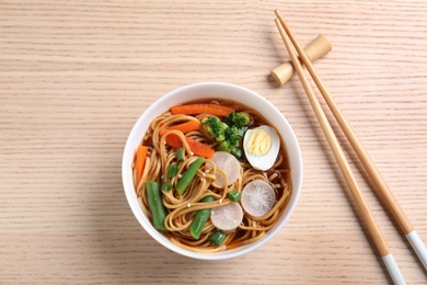 Photo of Tasty ramen with noodles, vegetables and chopsticks on wooden table, top view