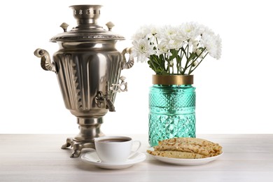 Photo of Vintage samovar, cup of hot drink, pancakes and vase with flowers on wooden table against white background. Traditional Russian tea ceremony