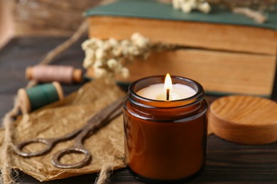 Photo of Burning scented candle, book and flowers on wooden table, closeup