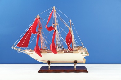 Miniature model of old ship with red sails on white table against blue background
