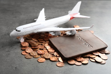 Pile of coins, passport and plane model on grey background
