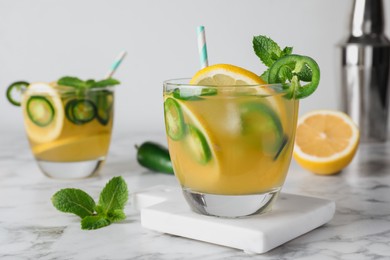 Spicy cocktail with jalapeno, lemon and mint on white marble table