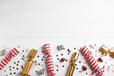 Christmas crackers with decorations and shiny confetti on white wooden background, flat lay. Space for text