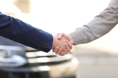 Salesman shaking hands with customer in modern auto dealership, closeup. Buying new car