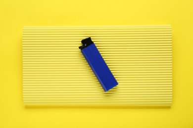 Photo of Stylish small pocket lighter with corrugated fiberboard on yellow background, top view