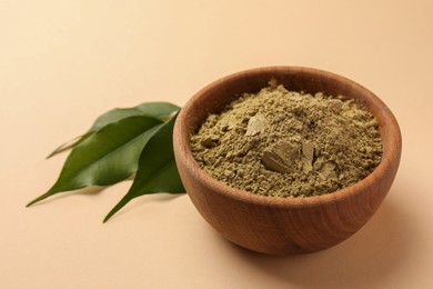 Photo of Henna powder and green leaves on beige background, closeup. Natural hair coloring