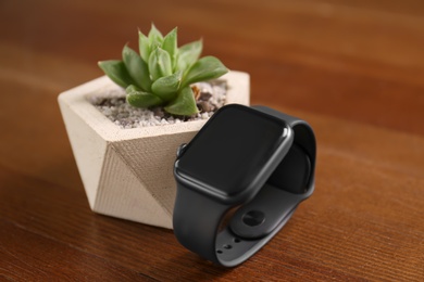 Stylish smart watch and plant on wooden table, closeup