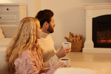 Photo of Lovely couple with hot drinks spending time together near fireplace at home