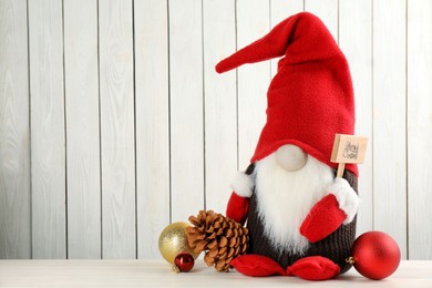 Cute Christmas gnome and festive decor on table against white wooden background. Space for text