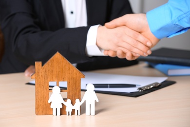 Man shaking hands with real estate agent at table, focus on family and house figures. Home insurance
