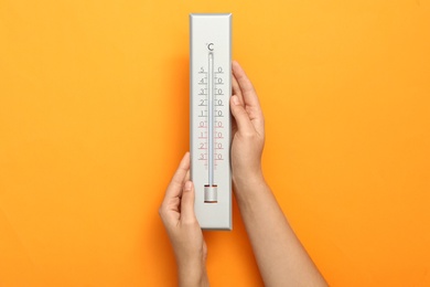 Woman with weather thermometer on orange background, closeup