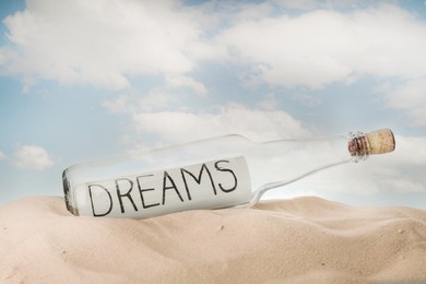 Corked glass bottle with Dreams note on sand against sky