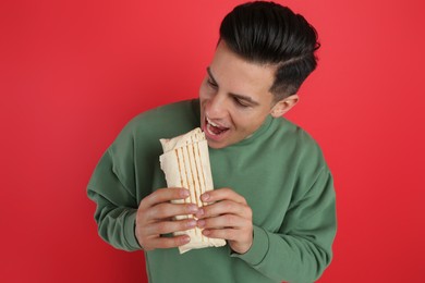 Man eating delicious shawarma on red background