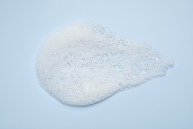 Photo of Spot of white washing foam on light blue background, top view