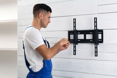 Professional technician with screwdriver installing TV bracket on wall indoors
