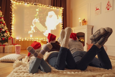 Family watching movie on projection screen in room decorated for Christmas. Home TV equipment
