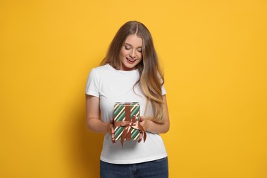 Emotional young woman holding colorful gift box on yellow background