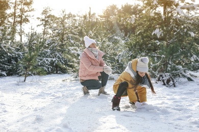 Mother and daughter rolling snowballs in winter forest