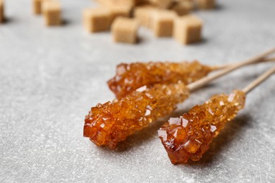Photo of Sticks with sugar crystals on light grey table, closeup. Tasty rock candies