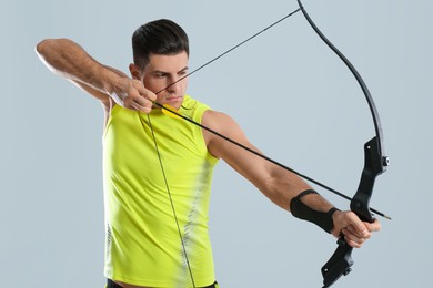 Man with bow and arrow practicing archery on light grey background