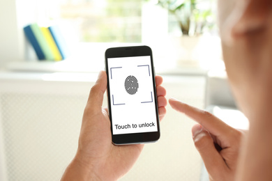 Man holding smartphone with fingerprint sensor indoors, closeup. Digital identity