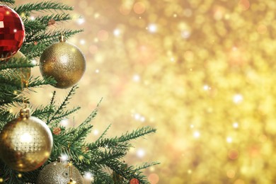 Beautiful Christmas tree with bright baubles on blurred golden background, closeup. Space for text