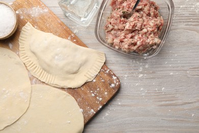 Photo of Raw chebureki with tasty filling and meat in bowl on wooden table, flat lay. Space for text