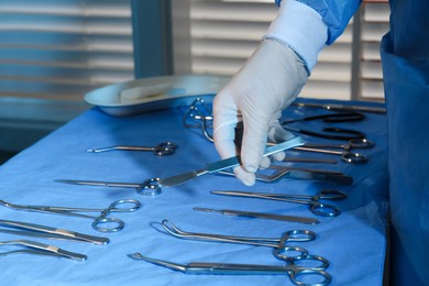 Doctor taking scalpel from table with different surgical instruments indoors, closeup