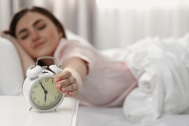 Photo of Young woman turning off alarm clock at home in morning, focus on hand. Space for text