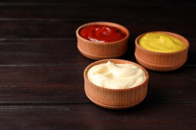 Ketchup, mustard and mayonnaise in bowls on wooden table, space for text