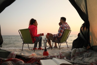 Couple resting near sea at sunset, view from camping tent