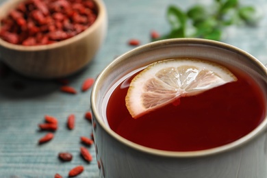 Healthy goji tea with lemon in cup on blue wooden table, closeup