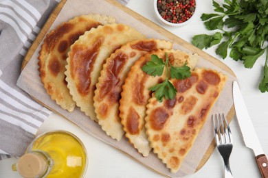 Delicious fried chebureki and parsley served on white table, flat lay