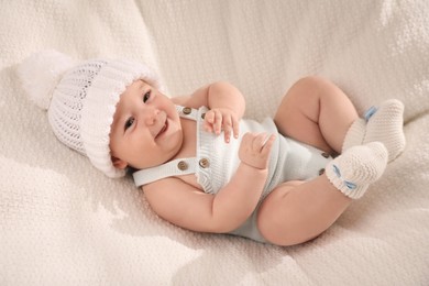 Photo of Cute little baby wearing white warm hat on knitted blanket