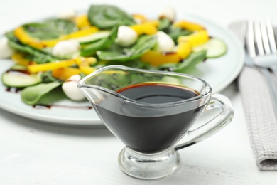 Balsamic vinegar in glass gravy boat near plate with vegetable salad on table, closeup