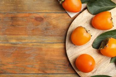Delicious fresh persimmons and green leaves on wooden table, flat lay. Space for text