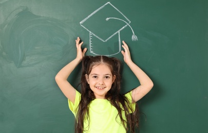 Little school child near chalkboard with drawing of graduate cap