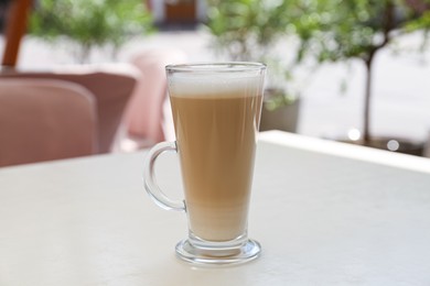 Photo of Glass with delicious coffee on white table in outdoor cafe