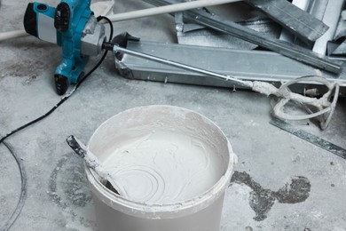 Bucket with plaster and putty knife near construction equipment on concrete floor