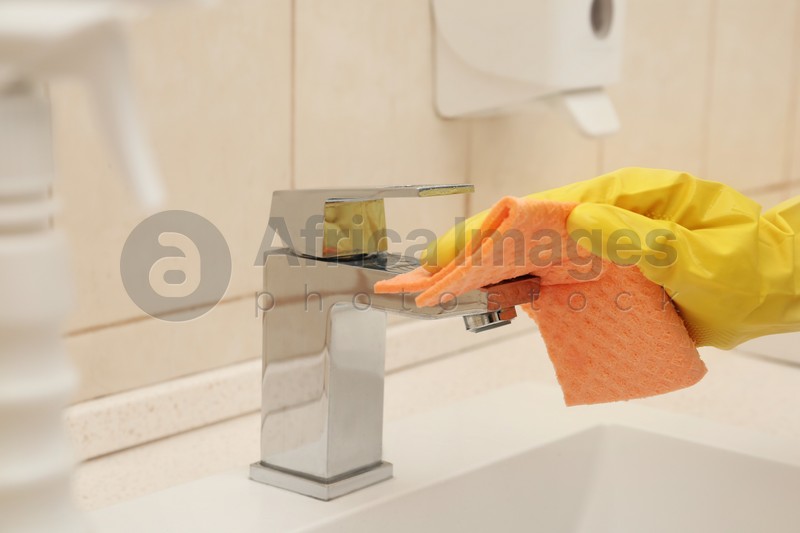 Person cleaning faucet with rag in bathroom, closeup